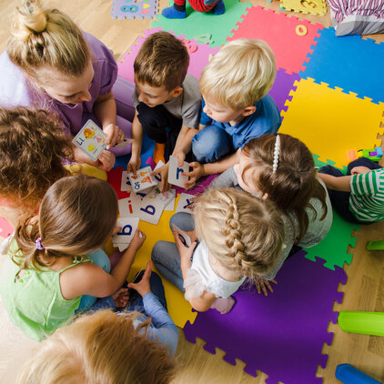 Group of kindergarten kids sitting closely on a floor together with teacher, providing group work. Children learning to cooperate while solving tasks.
